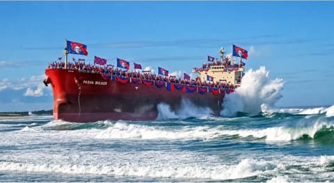 A red bulk carrier flying Knights flags pushing through heavy surf.