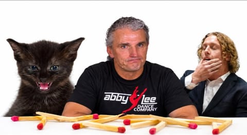 A hissing black kitten beside two men, with a row of snapped matchsticks in front of them.