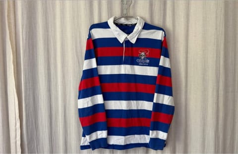 A red, white and blue striped rugby jersey with a Knights badge hanging in front of a cream curtain.