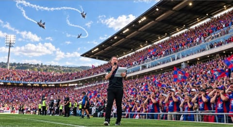 A man holding a microphone and papers on the field in front of a packed grandstand of fans, with jets trailing smoke across a blue sky.