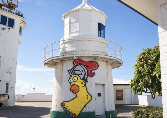 A cartoon chicken in a knight's helmet painted on the base of a white lighthouse.
